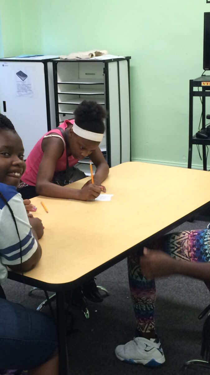 Two youth sitting around a table, one writing on a piece of paper