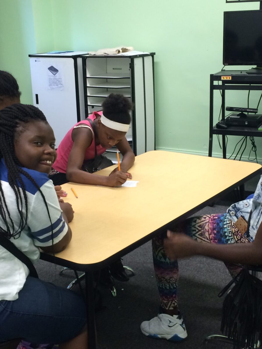 Two youth sitting around a table, one writing on a piece of paper