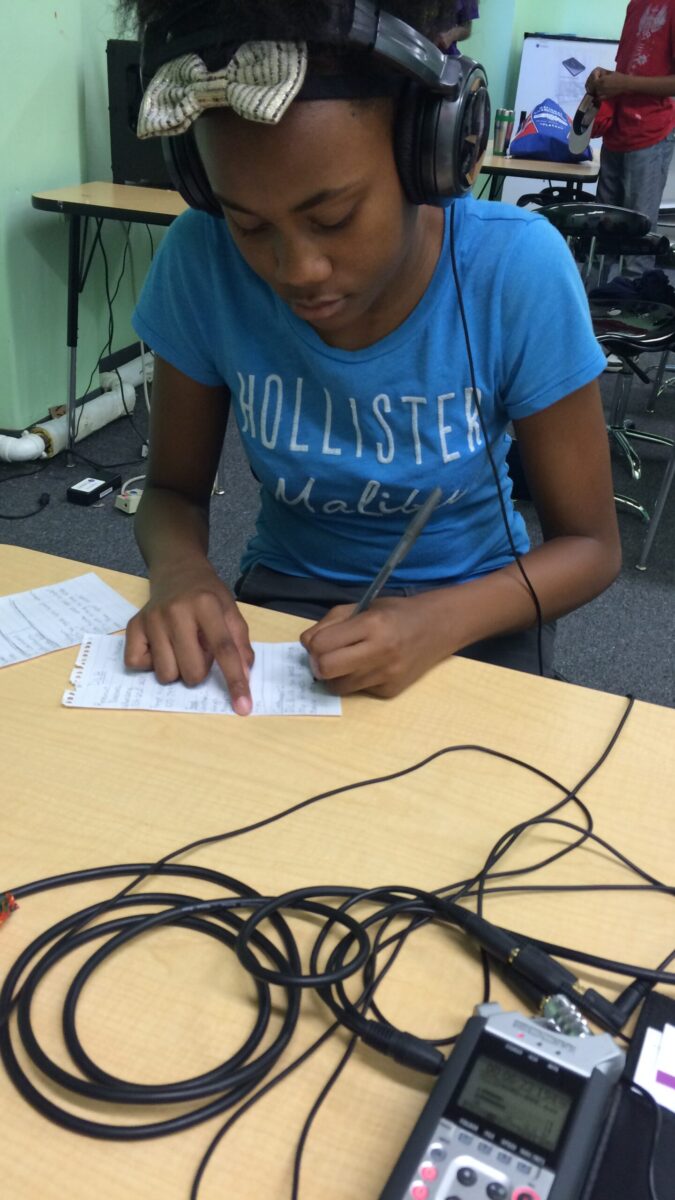 A teen wearing headphones writing on a piece of paper on a classroom desk