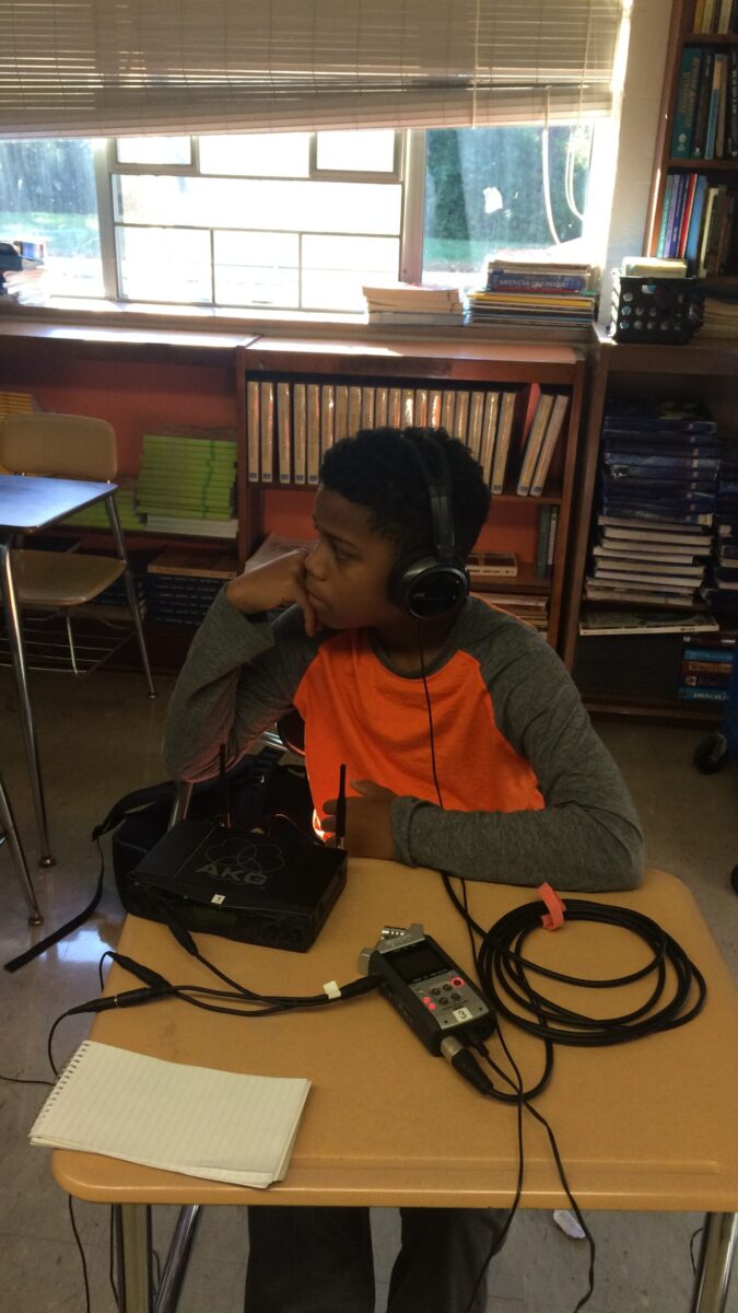 A youth wearing headphones sitting behind a portable recorder on a classroom desk