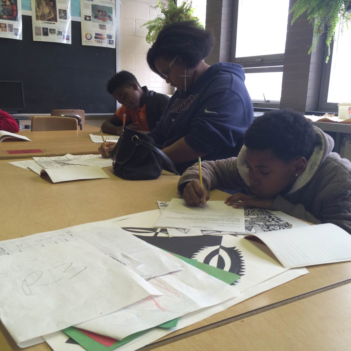 IMG_1071 Three youth writing on pieces of paper on a classroom desk