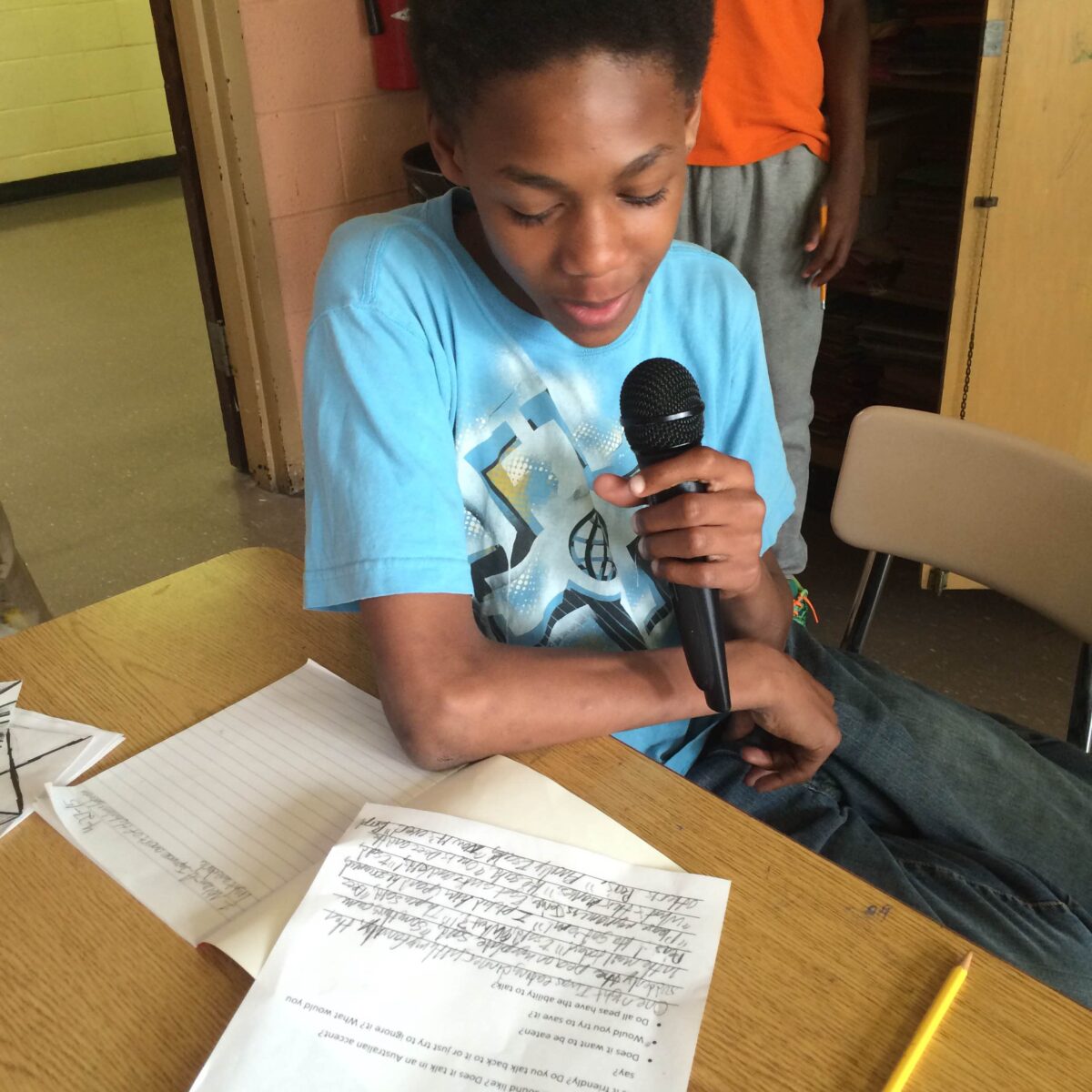 IMG_1084 A youth holding a microphone and looking down at a piece of paper on a classroom desk