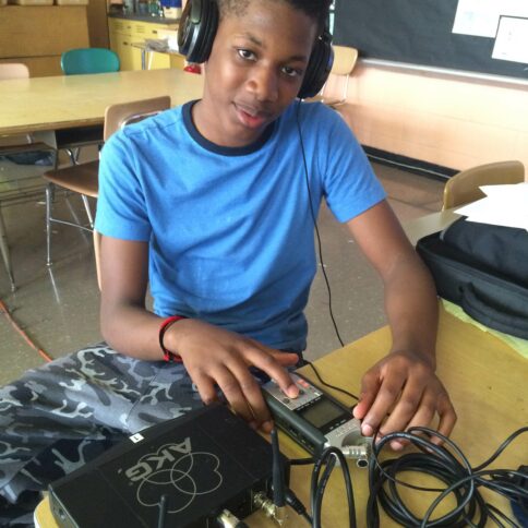 A youth wearing headphones interacting with a portable recorder on a classroom desk