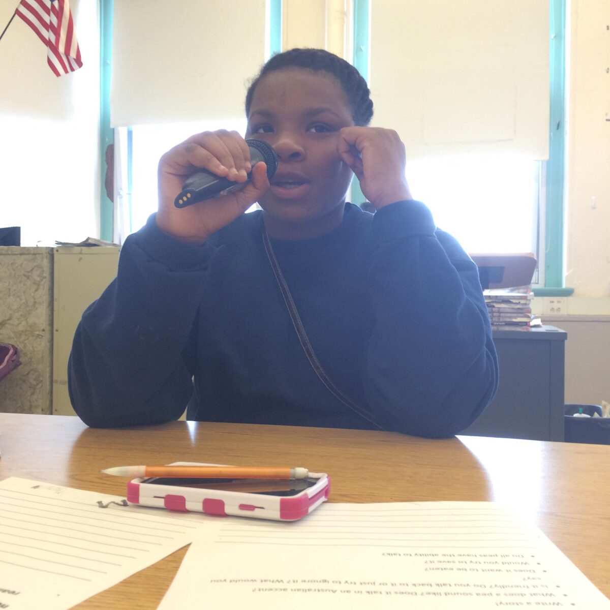 IMG_1089 A youth holding and speaking into a microphone sitting at a classroom desk