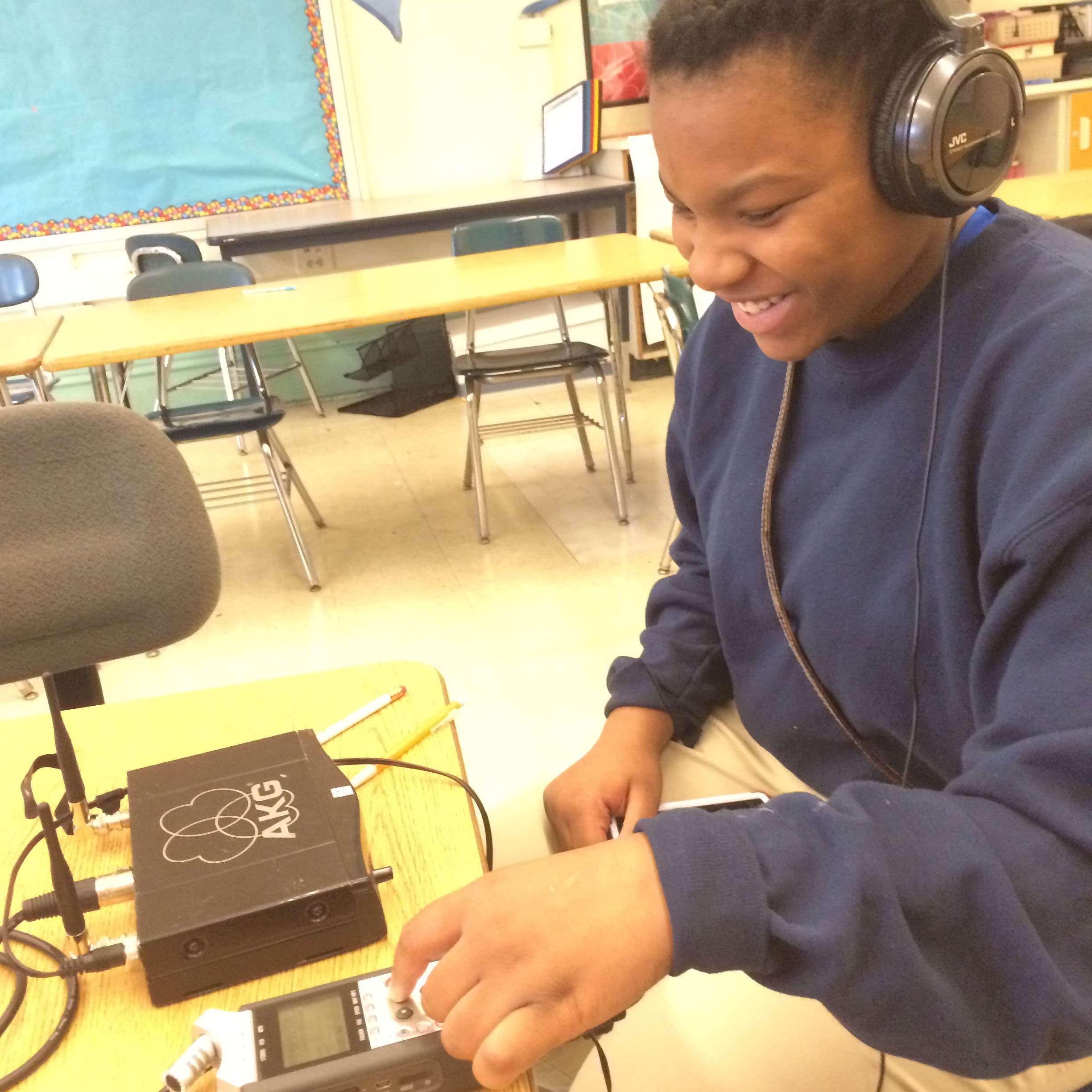 A youth wearing headphones smiling and interacting with a portable recorder on a classroom desk