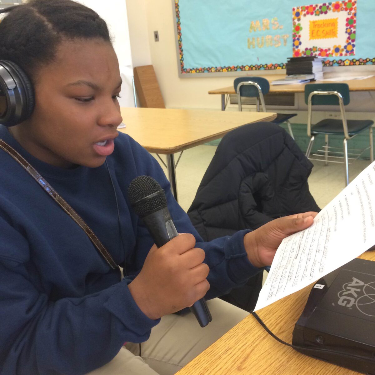 A youth wearing headphones holding a piece of paper and speaking into a microphone
