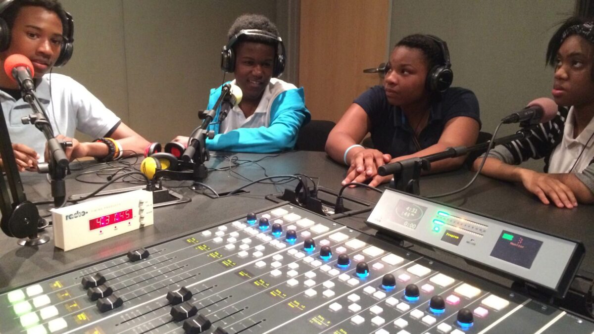 IMG_1125 Four youth wearing headphones speaking into microphones in a radio studio