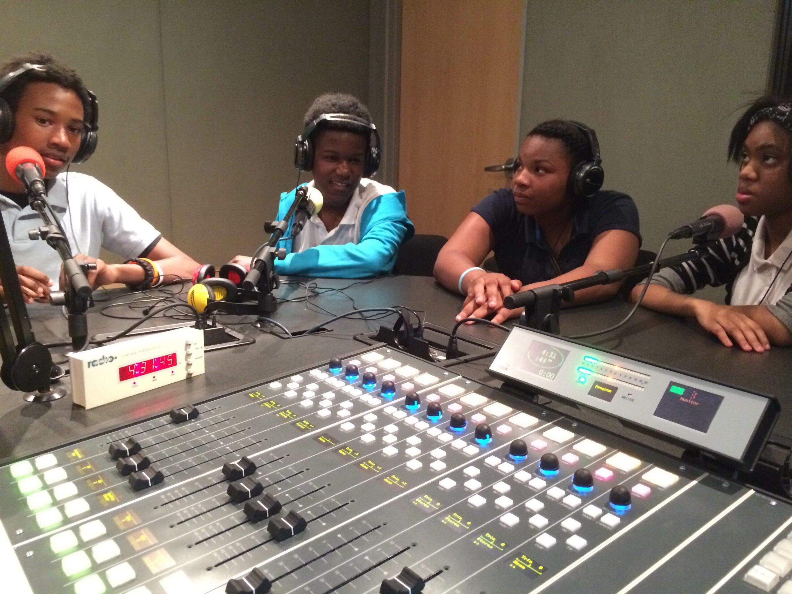 Four youth wearing headphones speaking into microphones in a radio studio