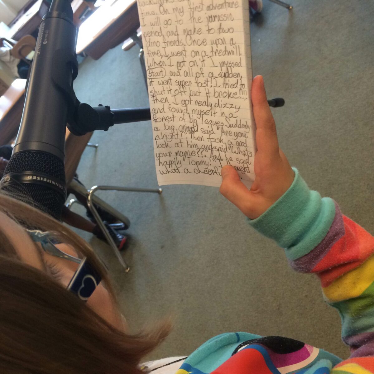 A youth holding a notepad standing behind a microphone in a classroom