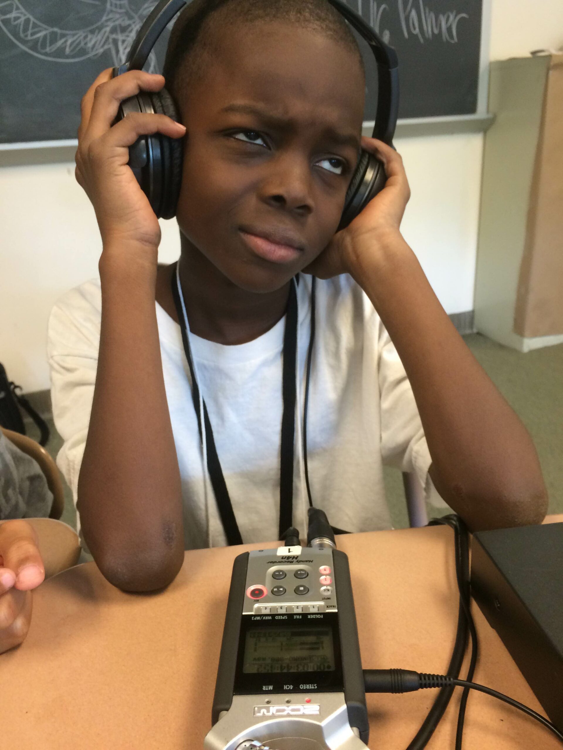 A youth wearing headphones listening to a portable recorder sitting at a classroom desk