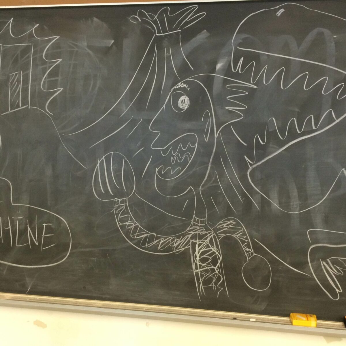 A chalkboard with a drawing of a creature and a dinosaur in front of a volcano, as well as a box labeled "time machine"