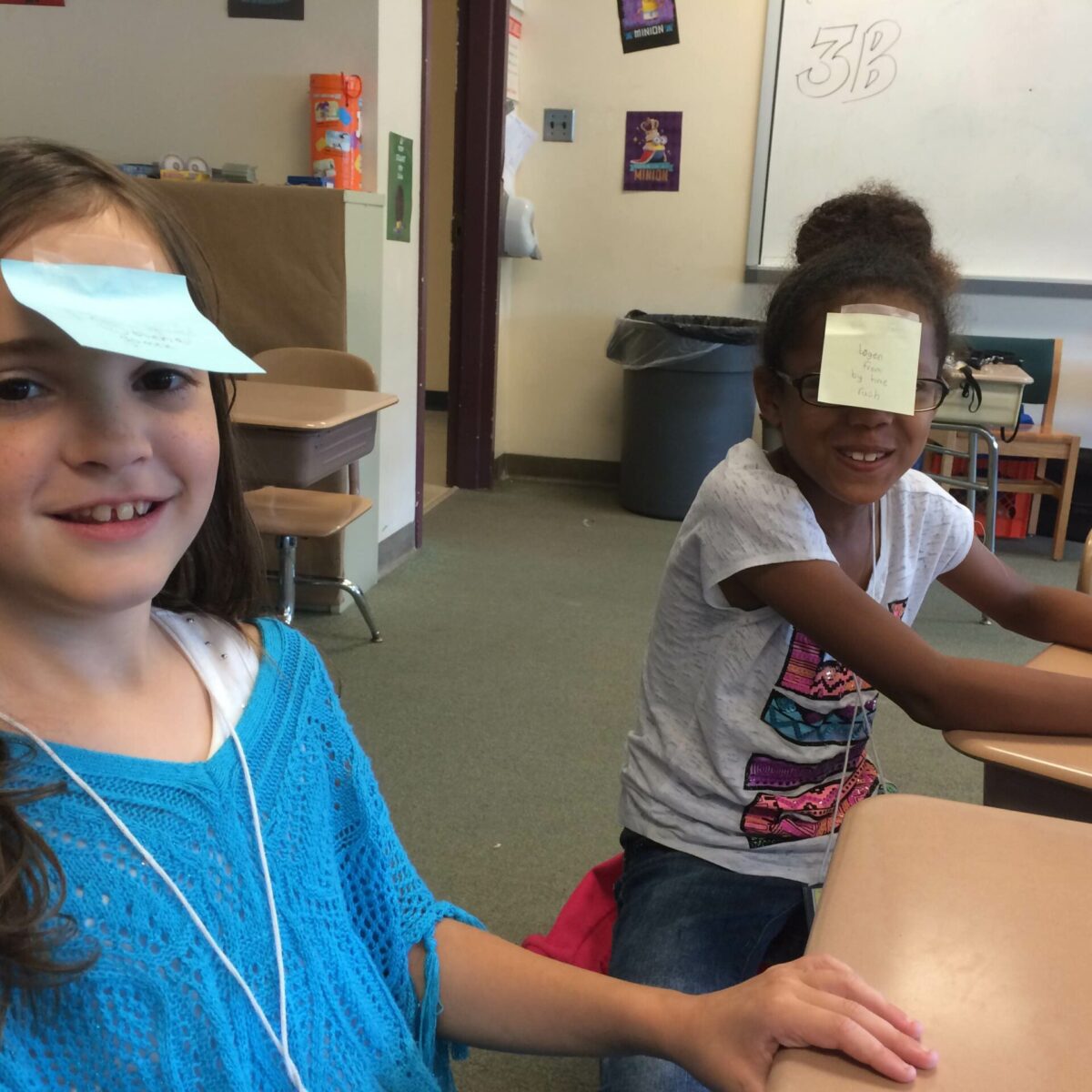 Two youth with post it notes on their heads sitting at classroom desks