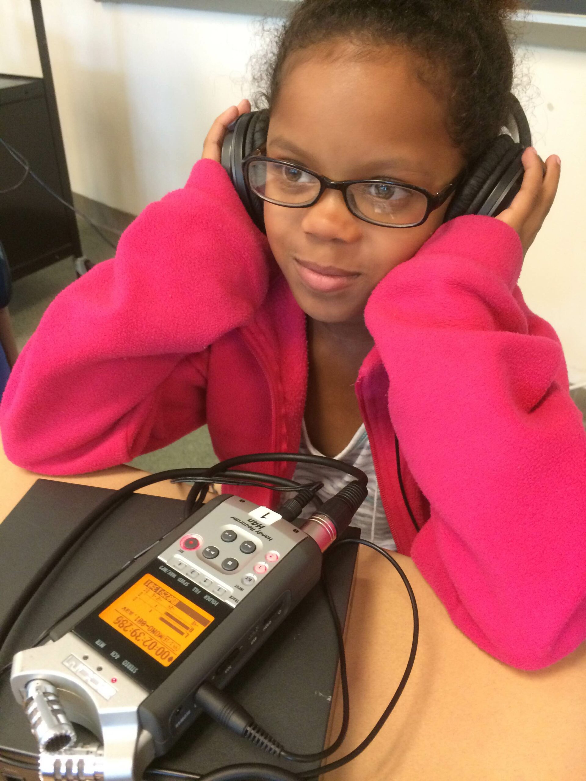 A youth wearing headphones listening to a portable recorder on a classroom desk