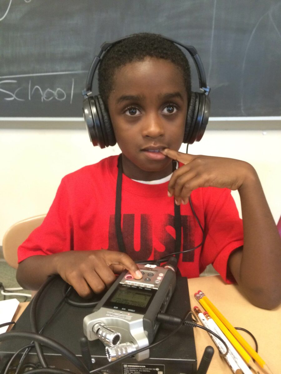 A youth wearing headphones listening to a portable recorder on a classroom desk