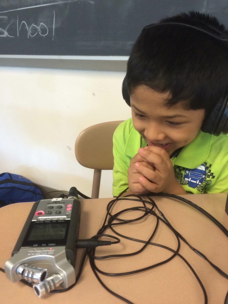 AA youth wearing headphones listening to a portable recorder on a classroom desk