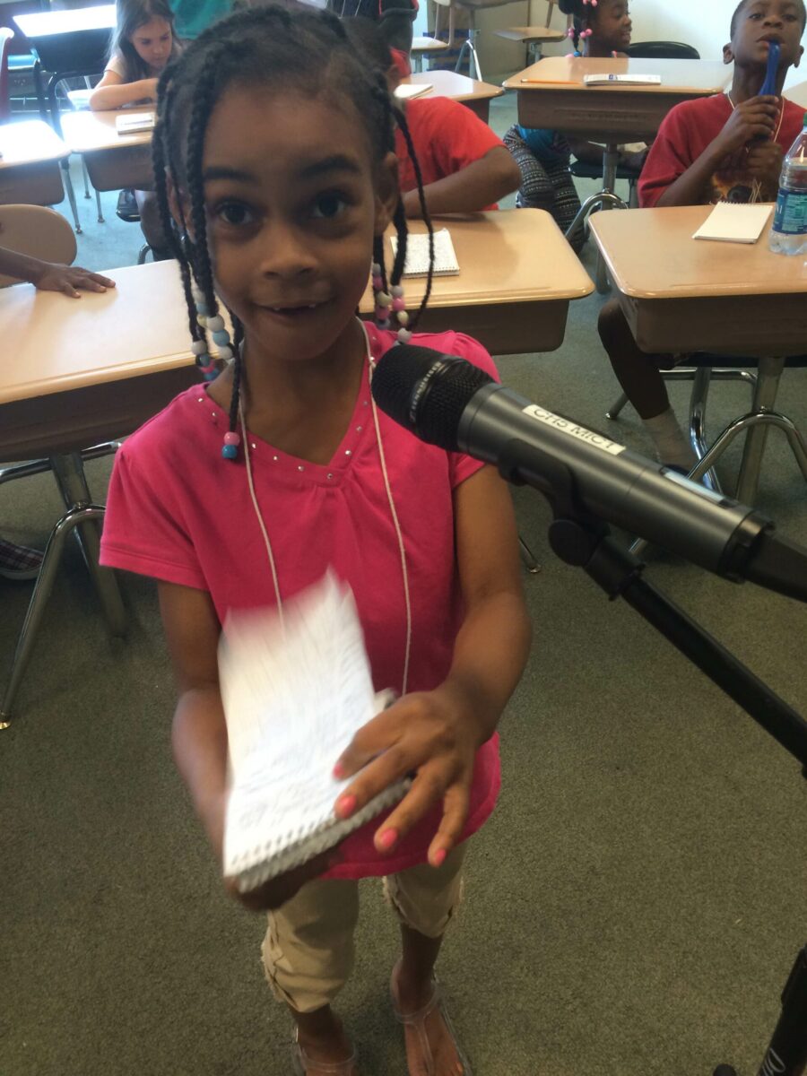 A youth holding a notepad standing behind a microphone in a classroom