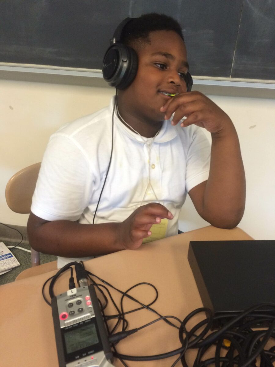 A youth wearing headphones listening to a portable recorder on a classroom desk