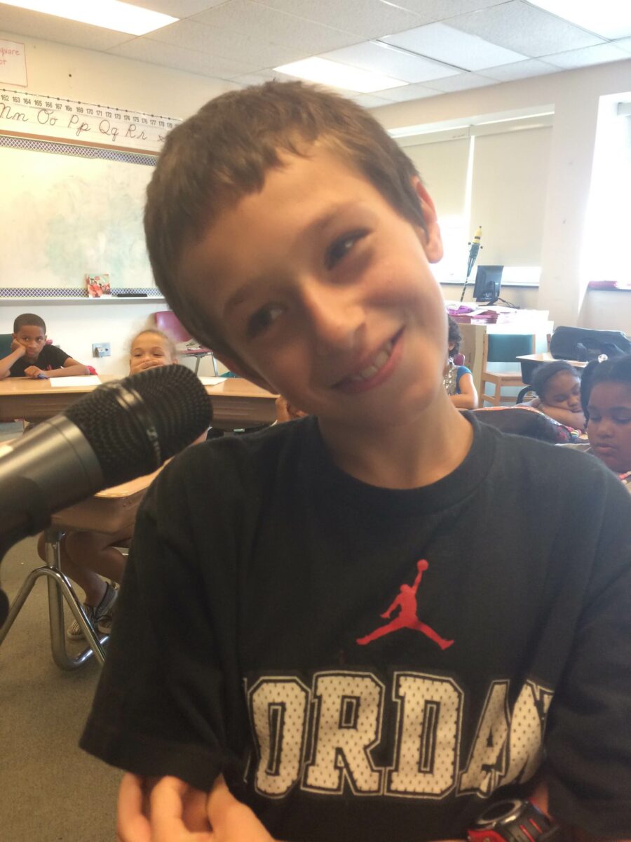 A youth smiling while standing behind a microphone in a classroom
