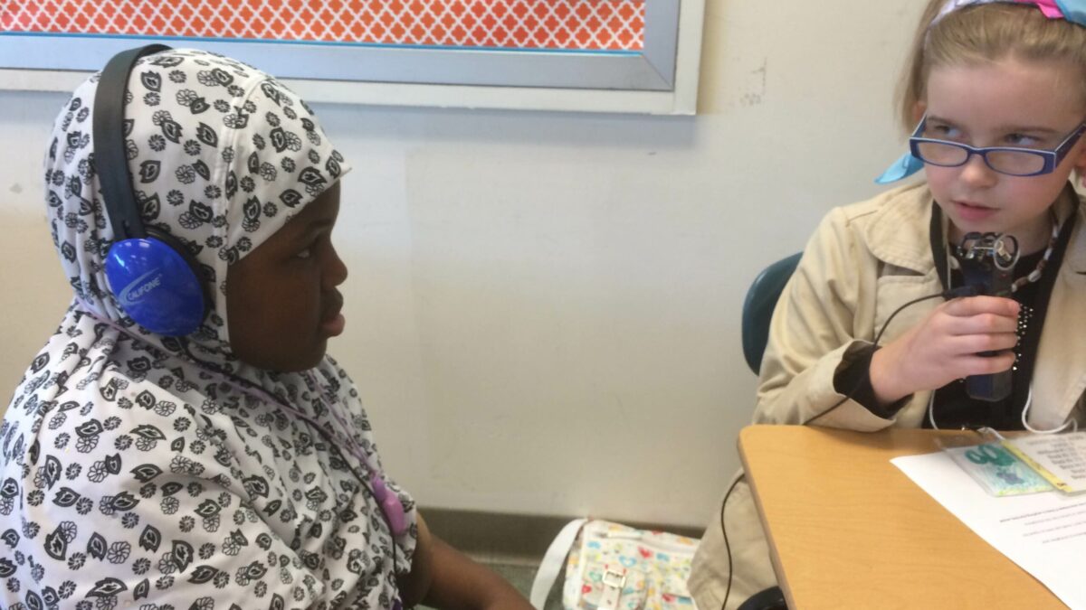 IMG_1392 A youth wearing headphones listening to another youth speaking into a portable recorder in a classroom