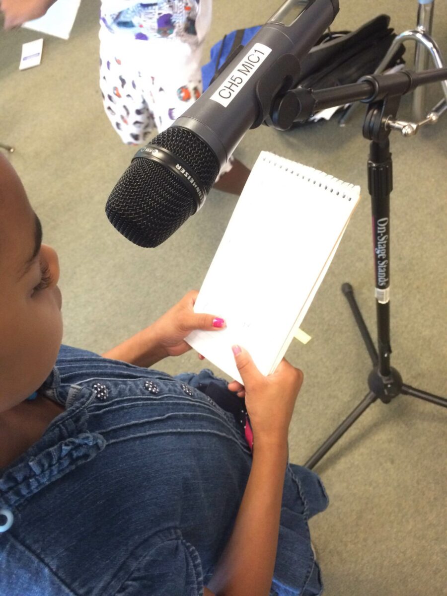 A youth holding a notepad and standing behind a microphone