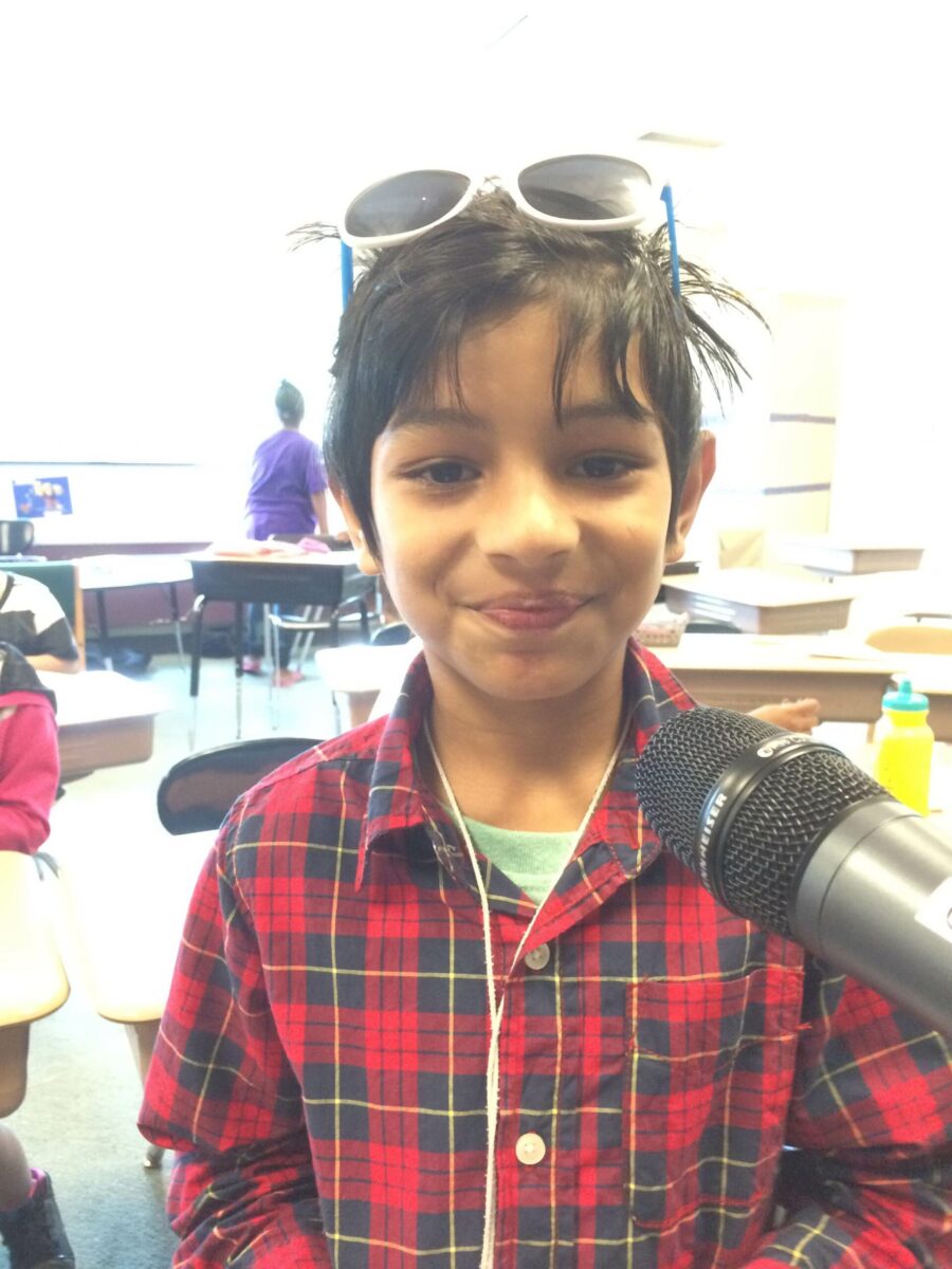 A youth smiling and standing behind a microphone in a classroom