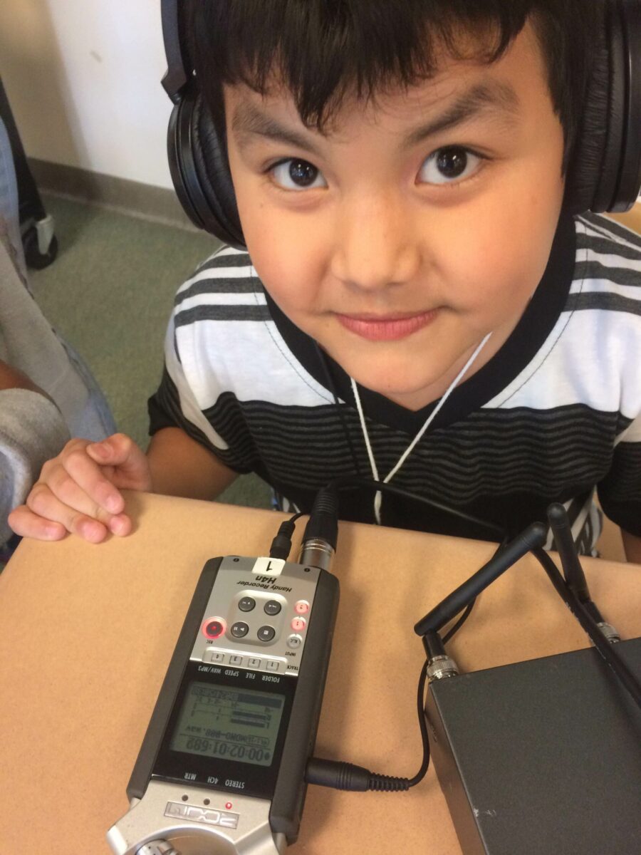 A youth wearing headphones sitting behind a portable recorder on a classroom desk