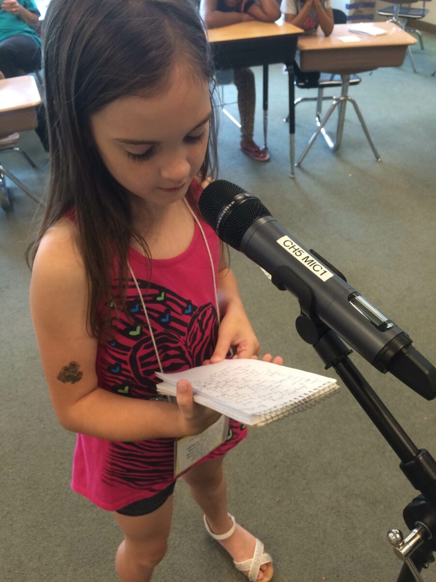 A youth holding a notepad and speaking into a microphone in a classroom