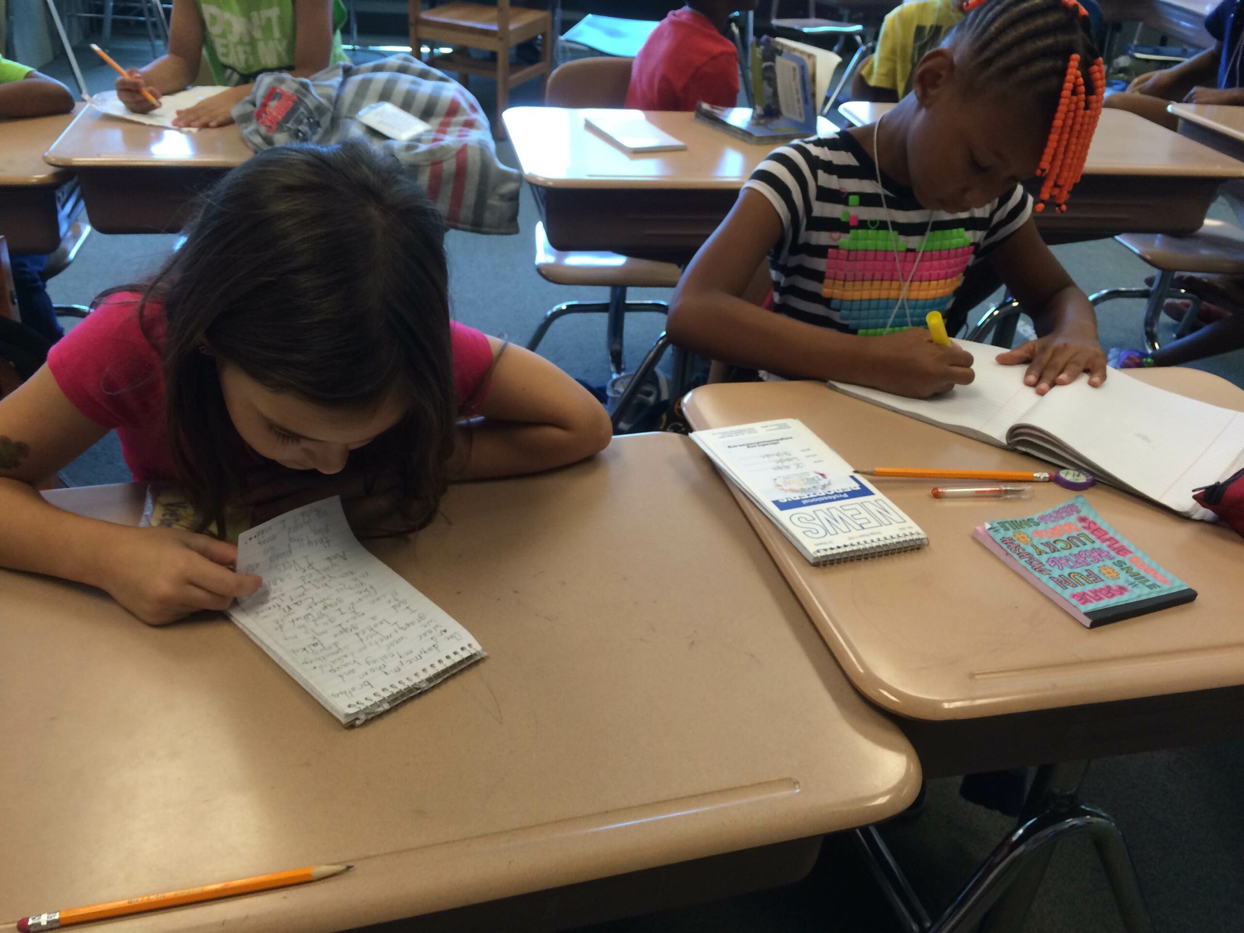 Two youth writing onto notepads on classroom desks