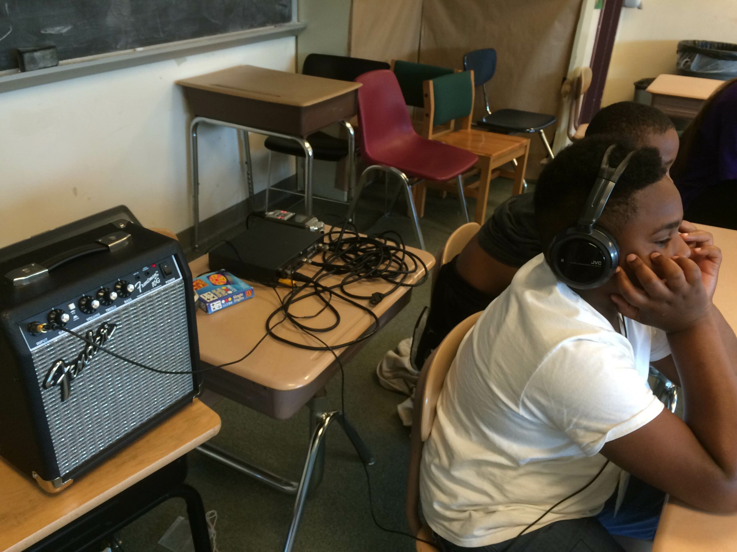 A youth wearing headphones sitting with their head in their hands on a classroom desk