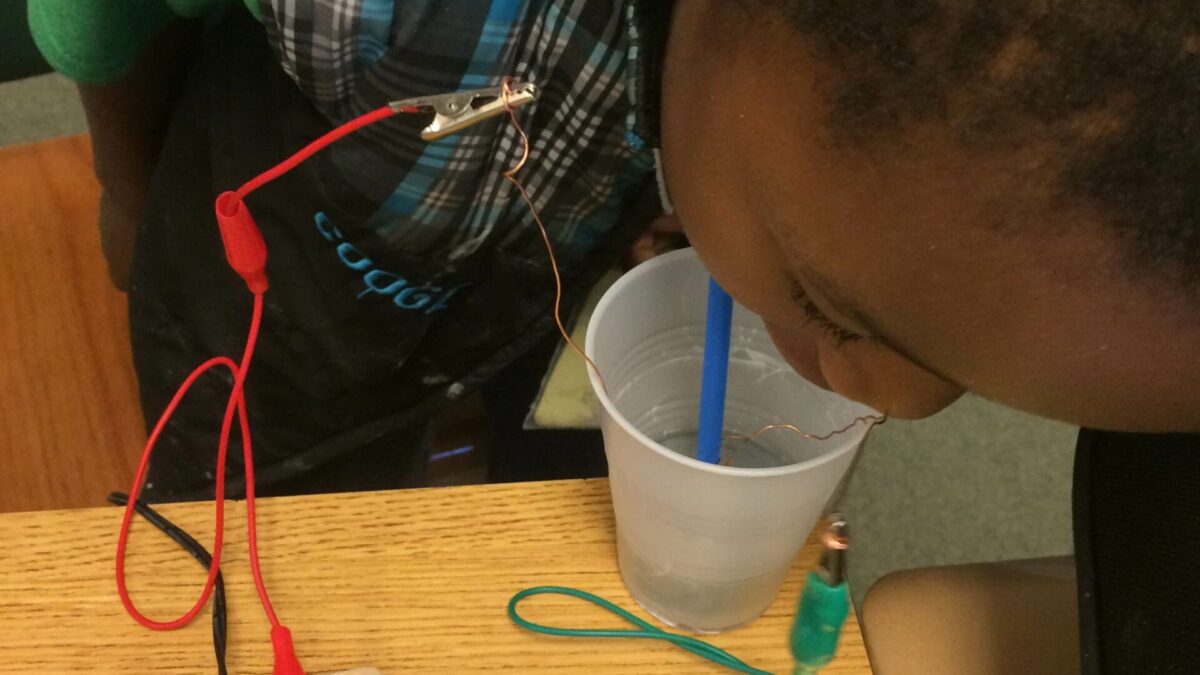 A youth putting their face into a plastic cup connected to a portable recorder on a wooden table