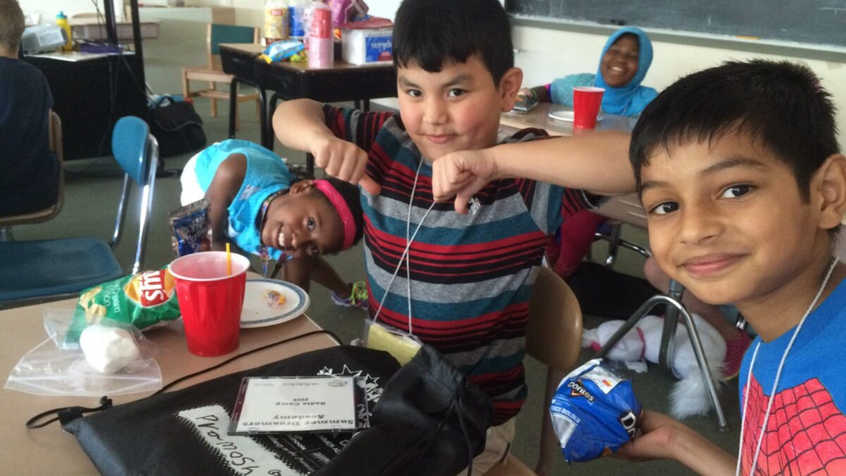 Three youth smiling and posing sitting around classroom desks
