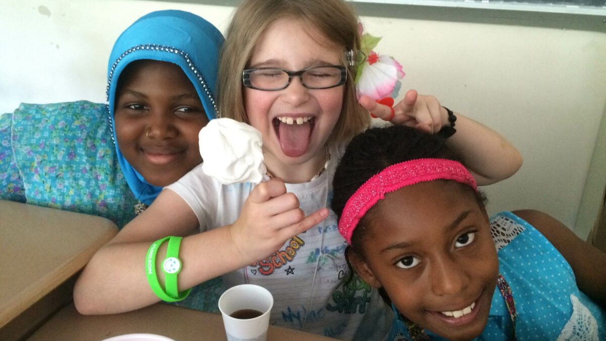 Three youth smiling and posing sitting around classroom desks