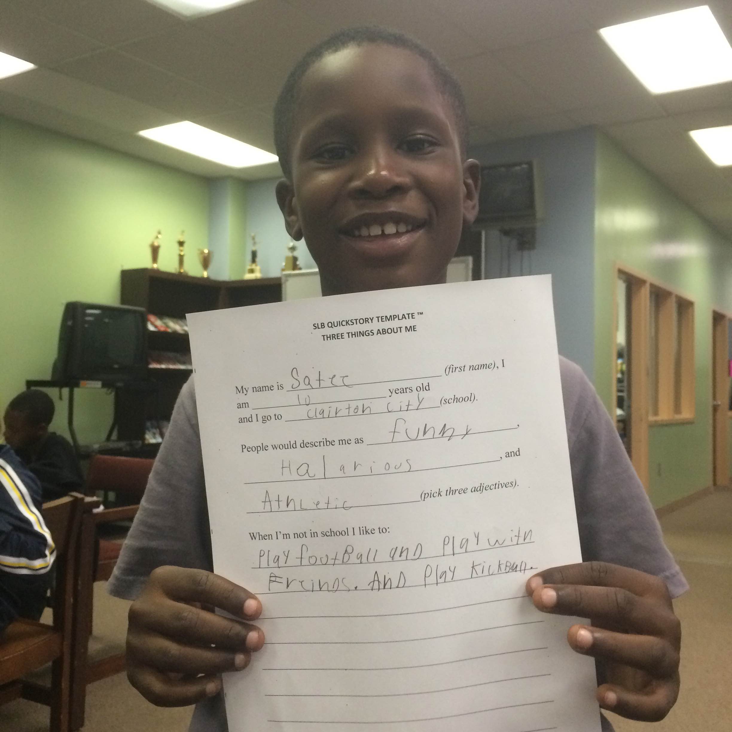 A youth holding up a piece of paper and smiling in a library