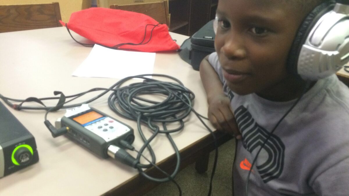 A youth wearing headphones sitting behind a portable recorder on a table