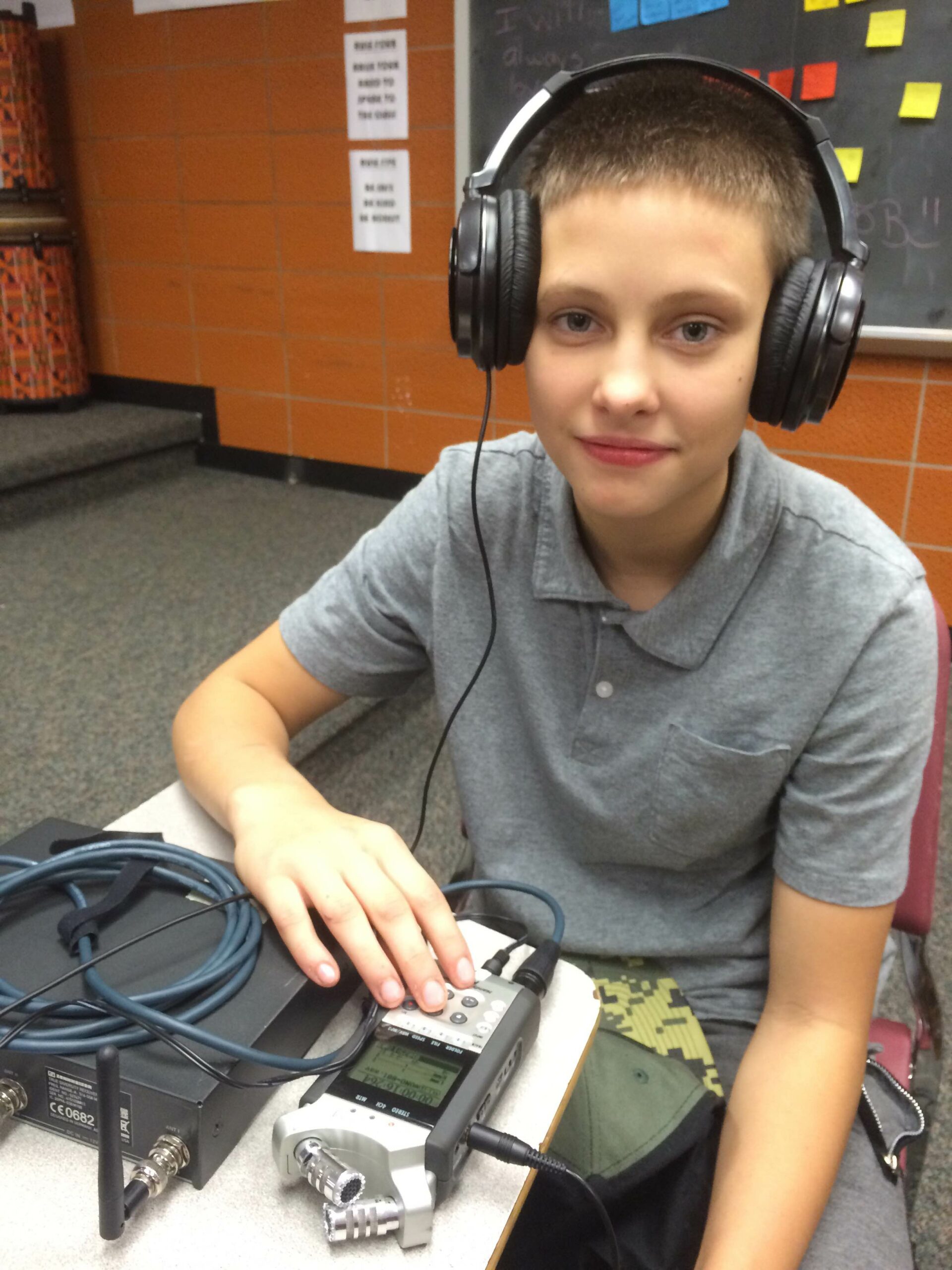 A youth wearing headphones interacting with a portable recorder in a classroom
