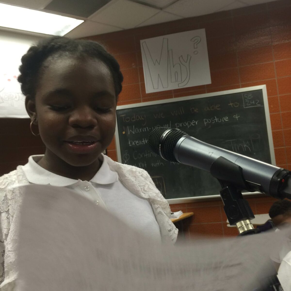 IMG_1863 A youth holding a piece of paper speaking into a microphone in a classroom