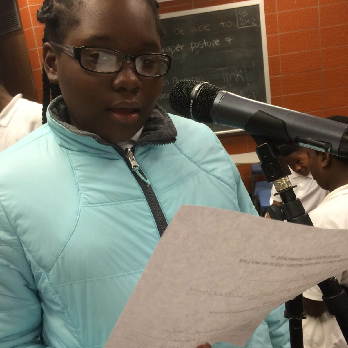 IMG_1865 A youth holding a piece of paper speaking into a microphone in a classroom