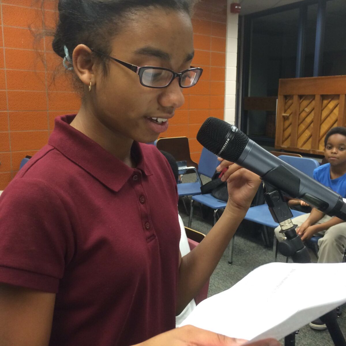 IMG_1867 A youth holding a piece of paper speaking into a microphone in a classroom