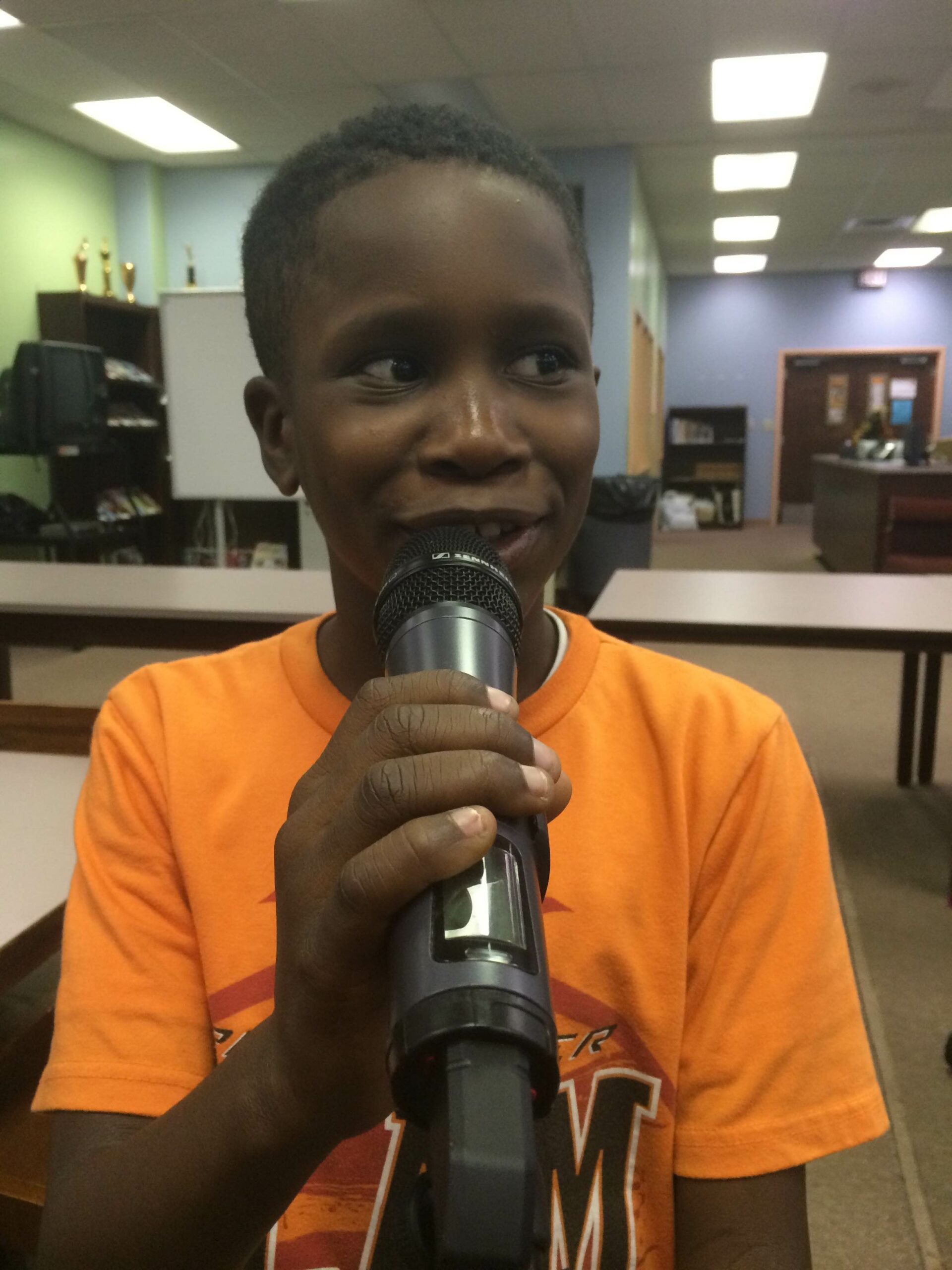A youth holding and speaking into a microphone in a library