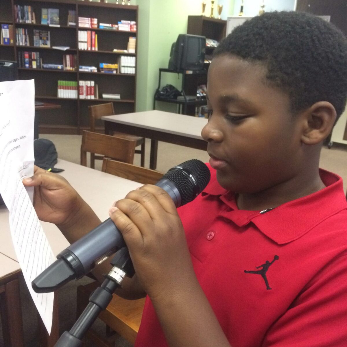 IMG_1879 A youth holding and speaking into a microphone and holding a piece of paper in a library