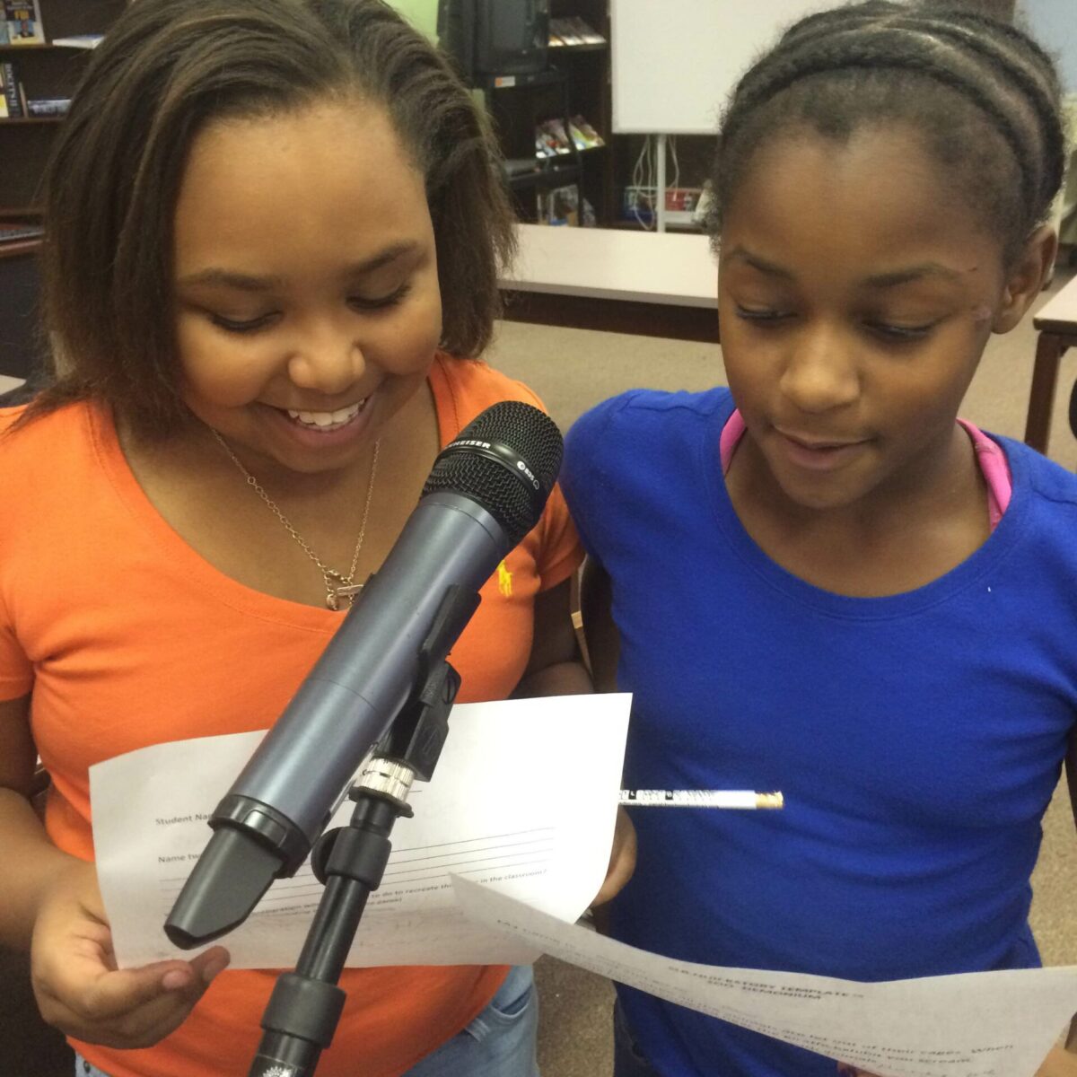 IMG_1881 Two youth holding pieces of paper speaking into a microphone in a library