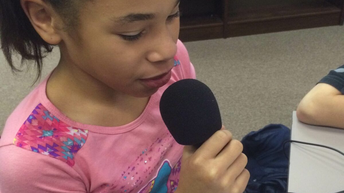 IMG_1981 A youth holding and speaking into a microphone sitting behind a gray table