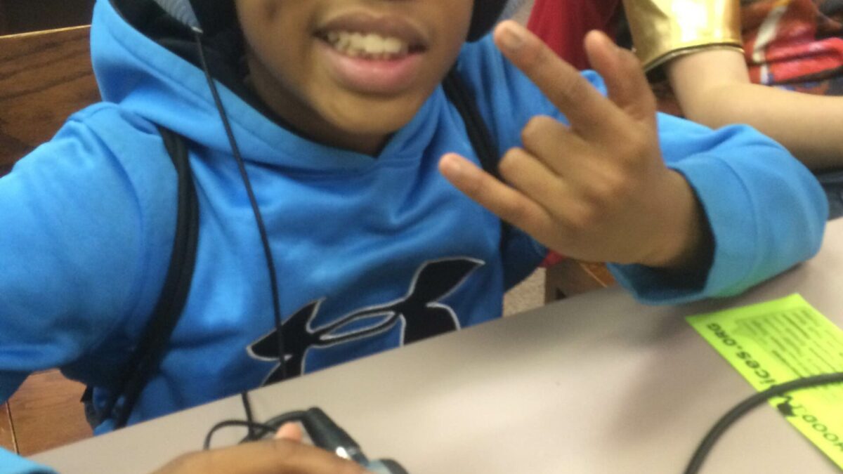 IMG_1985 A youth wearing headphones making a rocker sign with their hand and interacting with a portable recorder in a library