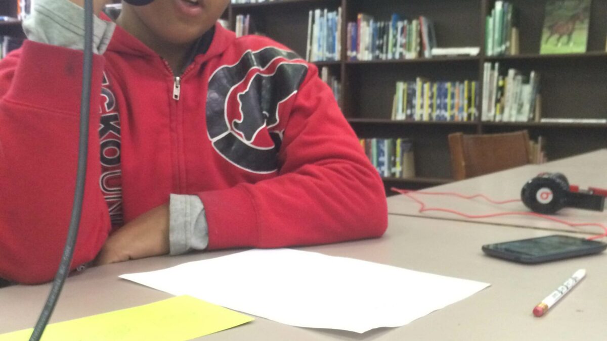 IMG_1987 A youth holding and speaking into a microphone looking down at a piece of paper on a table in a library