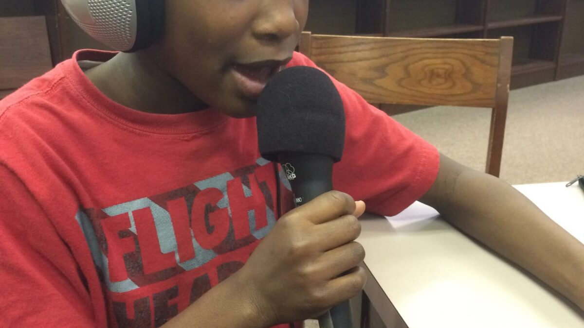 IMG_1993 A youth wearing headphones holding and speaking into a microphone in a library