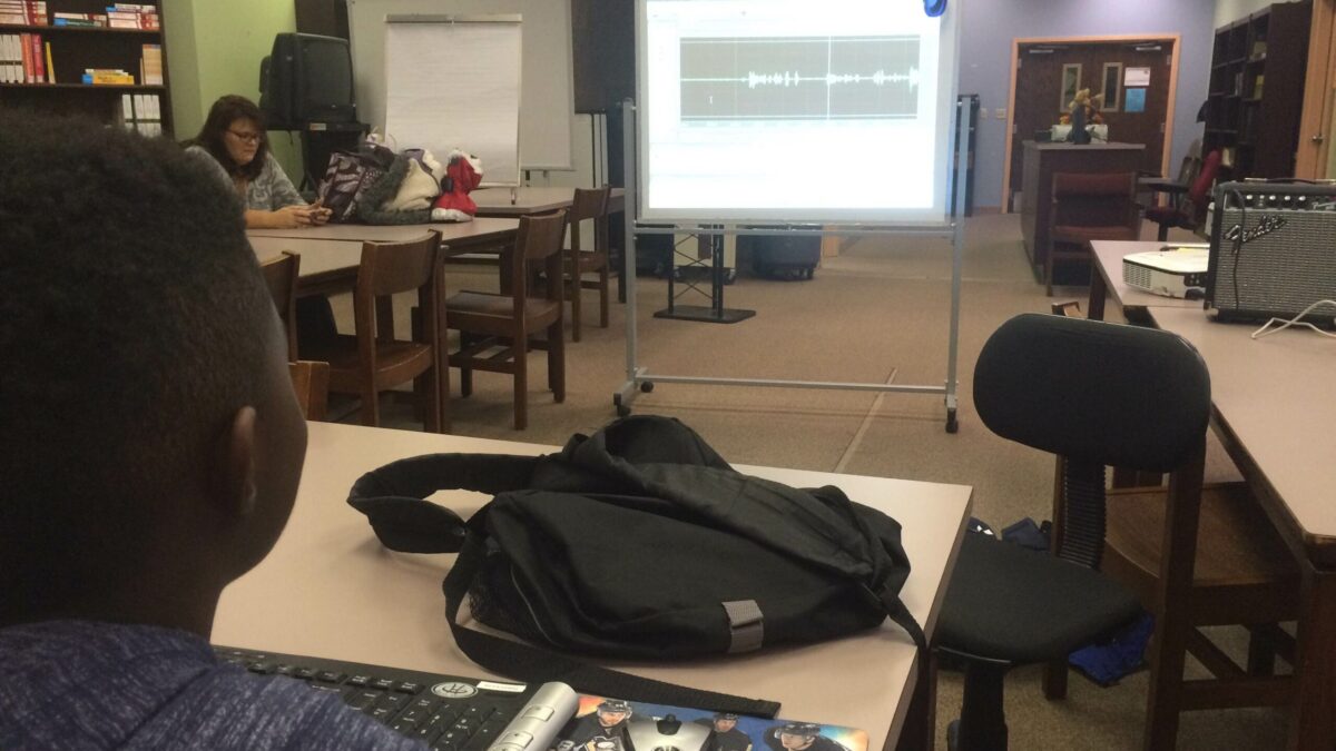 IMG_2015 A youth sitting at a table looking at a projected screen in a library