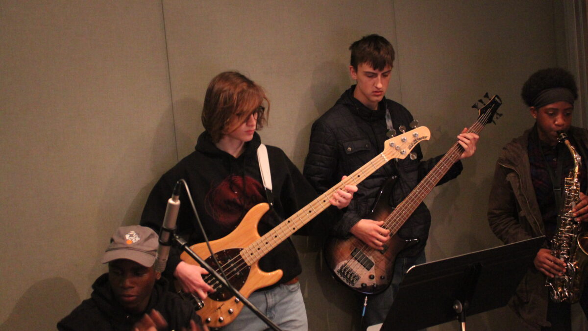 Two teens, one playing electric bass and one playing electric guitar, in a radio studio