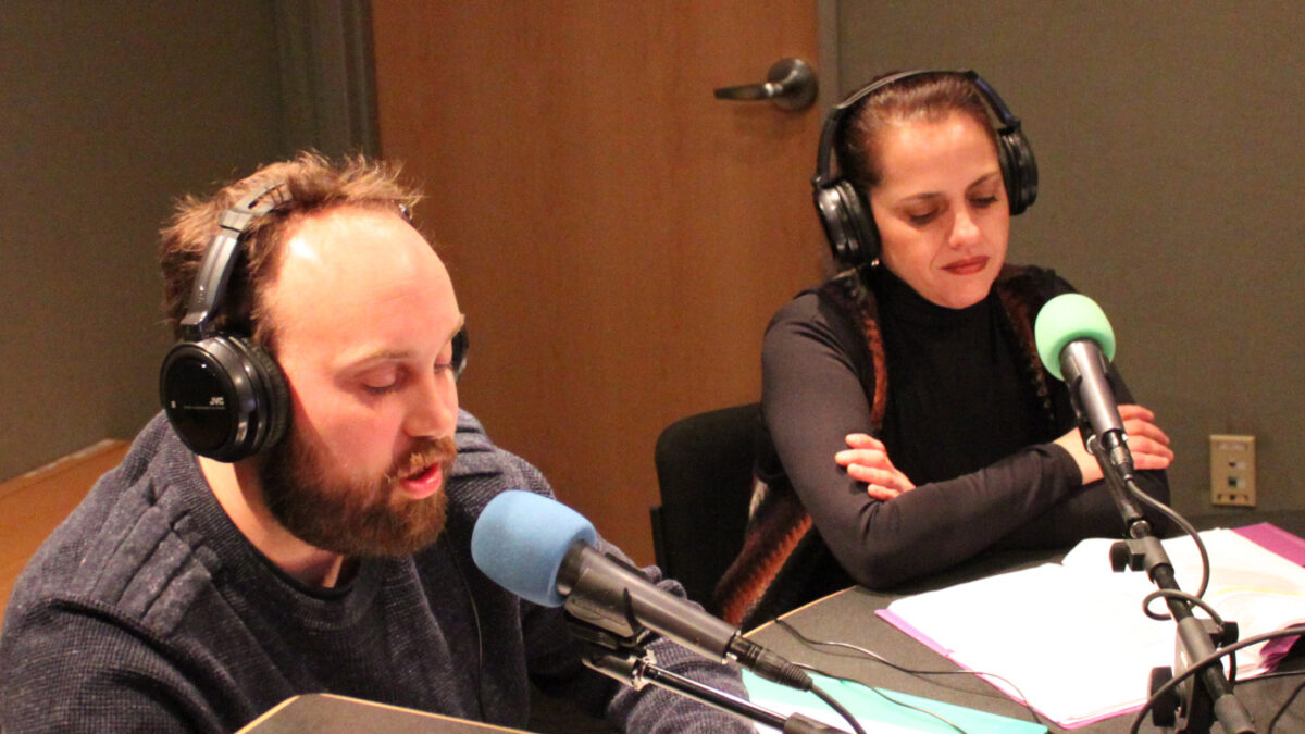 Two adults speaking into microphones in a radio studio