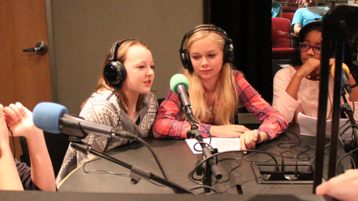 IMG_5115 Four youth wearing headphones speaking into microphones in a radio studio