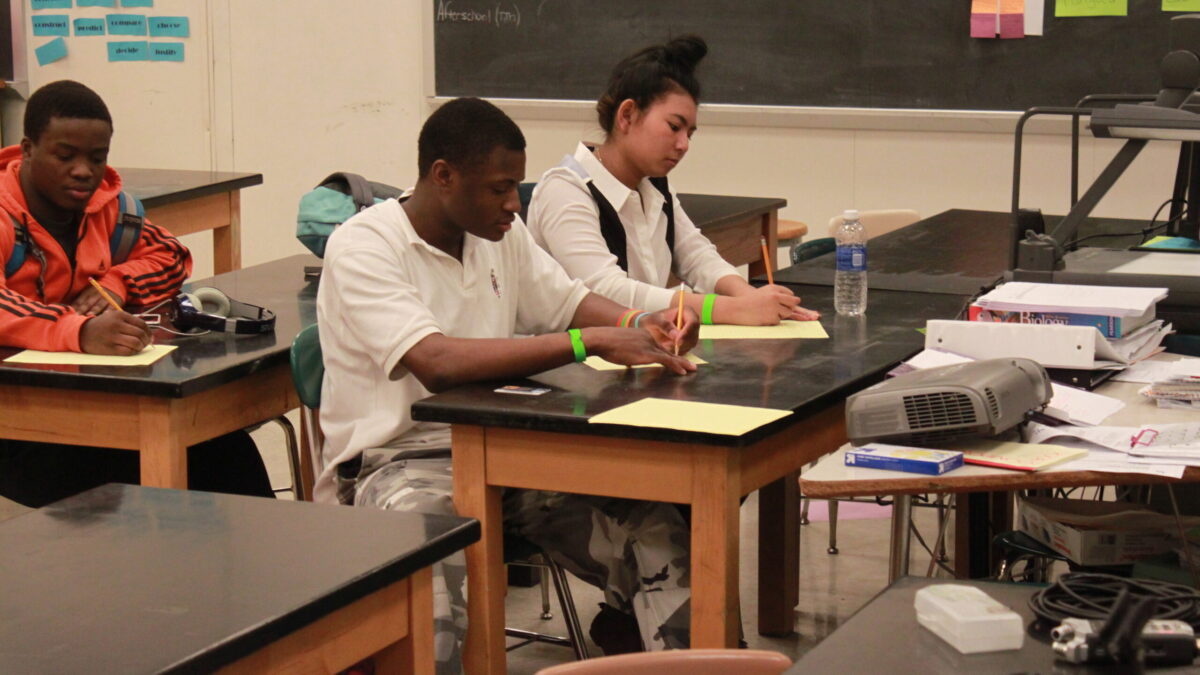 IMG_7804 Three teens writing on pieces of paper in a classroom